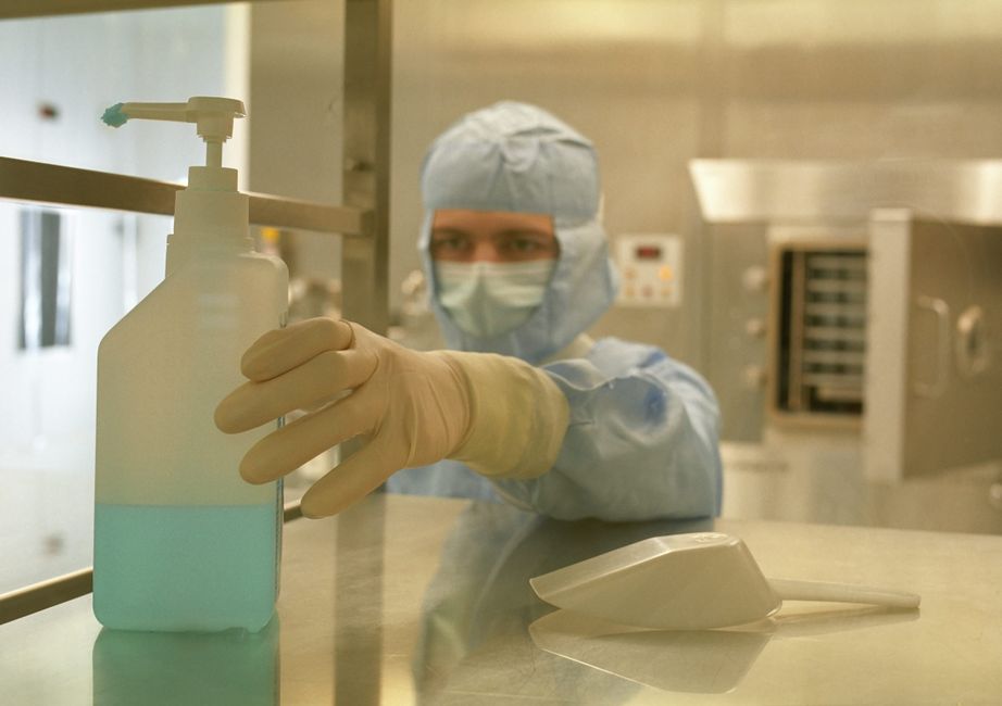A scientist in protective gear reaching for a sanitizer bottle in a laboratory setting.